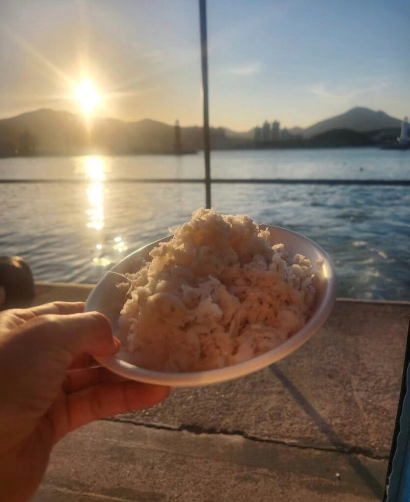 Fresh anago sashimi served outdoors at Hakri Breakwater with a Busan ocean sunset in the background