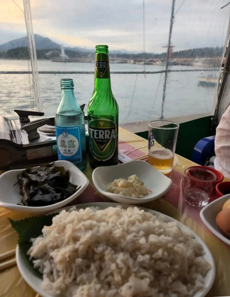 Fresh anago sashimi served outdoors at Hakri Breakwater with a Busan ocean sunset in the background