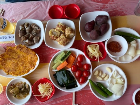 Generous complimentary banchan spread at Hakri Breakwater including kimchijeon, steamed sweet potato, and corn